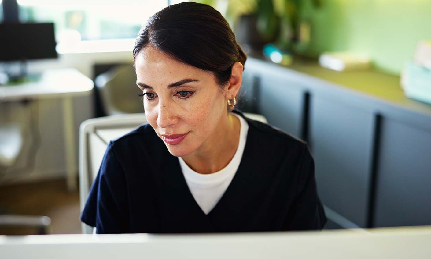 Person seated indoors looking toward a computer screen during a virtual meeting.
