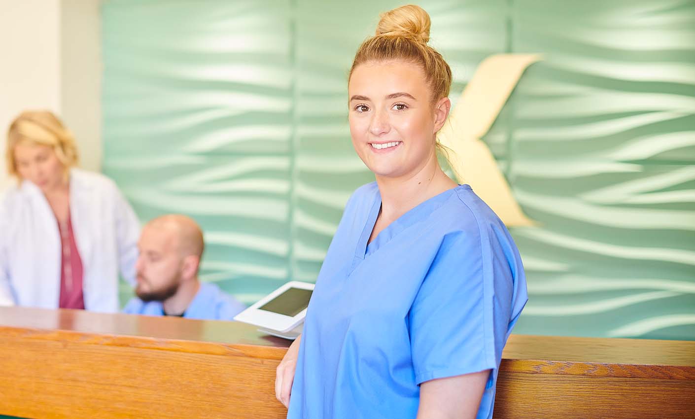 Healthcare worker in scrubs standing in a reception area.